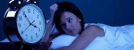 Femme éveillée dans son lit fixant un réveil en pleine nuit, par SANUSq Health sur l'insomnie chronique