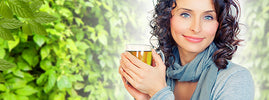 Femme souriante tenant une tasse d'infusion de jiaogulan devant un feuillage vert, adaptogène contre le stress – SANUSq Health
