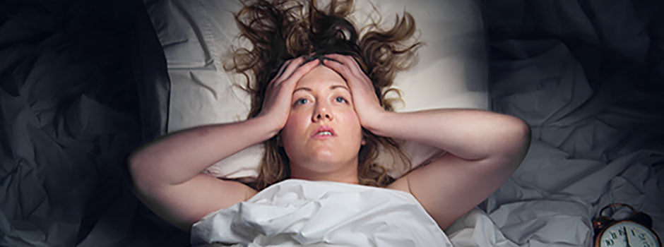 Femme insomniaque allongée, les mains sur la tête près d'un réveil, par SANUSq Health sur le magnésium et le sommeil