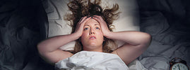 Femme insomniaque allongée, les mains sur la tête près d'un réveil, par SANUSq Health sur le magnésium et le sommeil