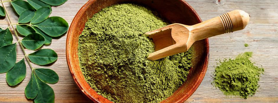 Bol de poudre de feuilles de moringa à côté de feuilles fraîches de moringa sur une table en bois rustique