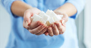 Femme tenant une poignée de morceaux de sucre blanc dans ses mains, les effets du sucre sur le corps – SANUSq Health