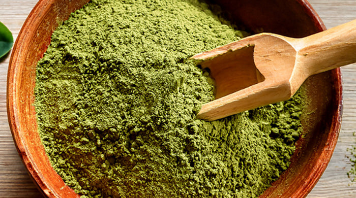 Bol de poudre de feuilles de moringa à côté de feuilles fraîches de moringa sur une table en bois rustique